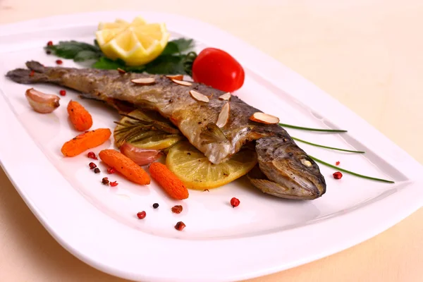 Fried trout with lemon and split almonds on white plate — Stock Photo, Image