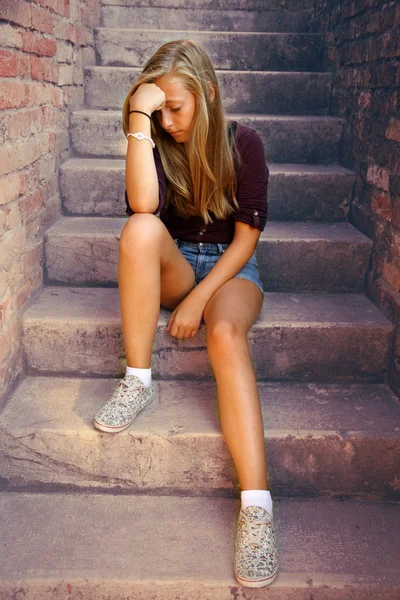 Thoughtful girl with blue eyes sitting at stone brick stairs