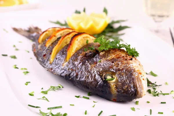 ızgara çipura balık, limon, roka beyaz plaka üzerinde