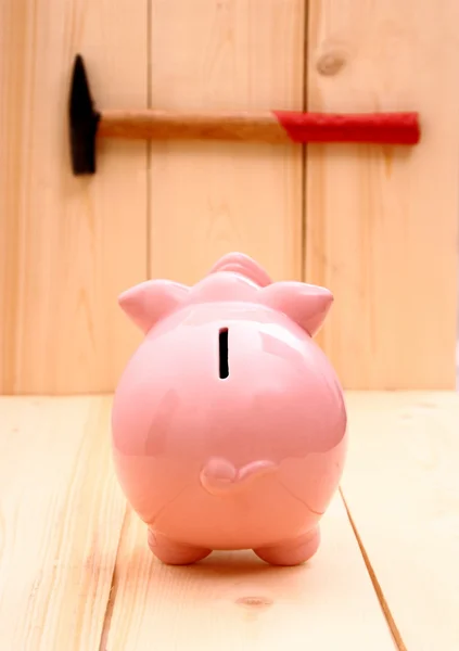 Funny pink piggy bank in focus and hammer on wood — Stock Photo, Image