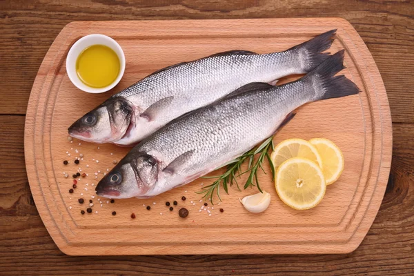 Dos peces morónidos frescos en tabla de cortar con ingredientes — Foto de Stock