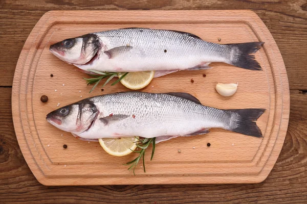 Dois peixes moronidae frescos em tábua de corte com ingredientes — Fotografia de Stock