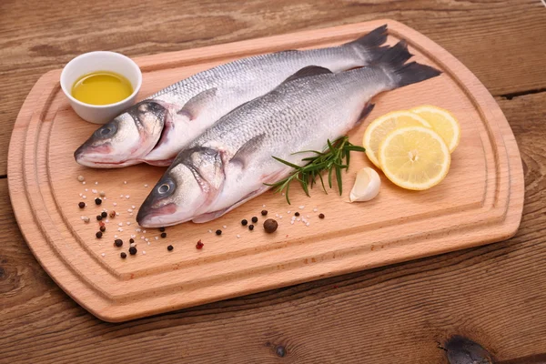 Two fresh sea bass fish on cutting board with ingredients — Stock Photo, Image