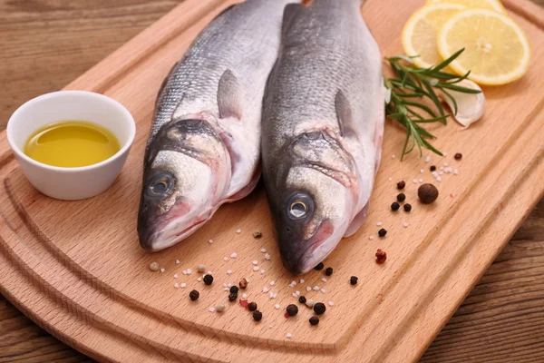 Dois peixes de robalo fresco na placa de corte — Fotografia de Stock