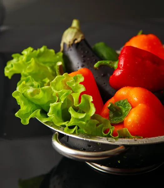 Freshly washed fresh vegetables in a metal colander isolated over black background. — Stock Photo, Image