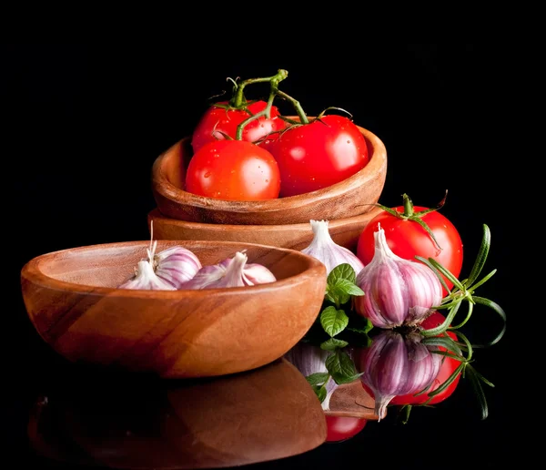 Tomatoes and garlic in wooden plate on black background. — Stock Photo, Image