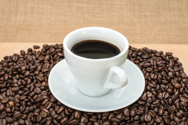 Leckerer Kaffee mit Kaffeebohnen im Hintergrund — Stockfoto