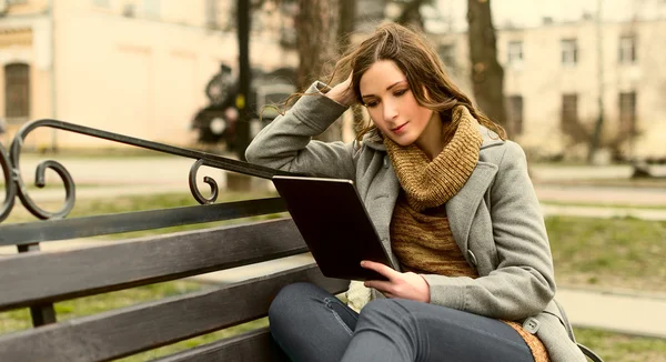Jovem mulher sentada com Tablet e leitura — Fotografia de Stock