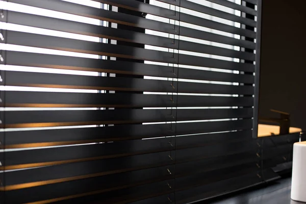 Ξύλινα blinds Coulisse μαύρο χρώμα closeup στο παράθυρο. Ξύλινη πλάκα πλάτους 50 mm. Βενετσιάνικες κουρτίνες στο μπάνιο. Μαύρη βρύση, καθρέφτης κοντά στο νιπτήρα. — Φωτογραφία Αρχείου