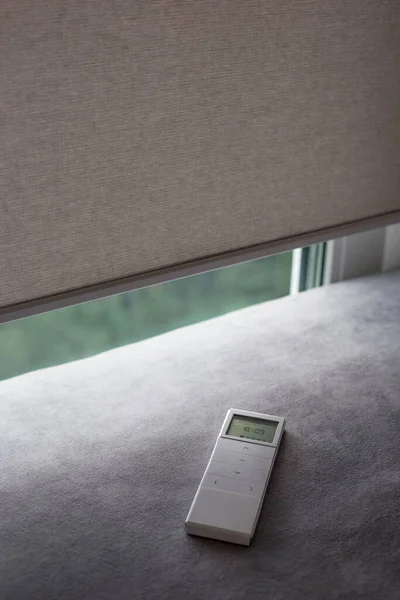 Motorlu patenler için beyaz uzaktan kumanda paneli. Otomatik silindirler camdaki bej rengi kör eder. Uzaktan kumandalı gölgeler kanepenin yanında. Uzaktan kumanda koltukta..