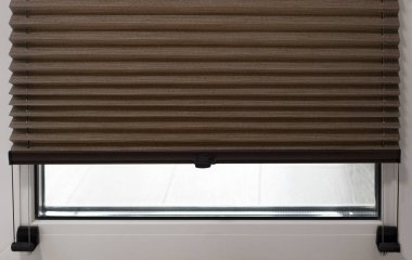 Pleated blinds close up on the window in the interior. Home blinds - cordless pleated modern shades on apartment windows. Brown color fabric.