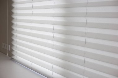 Pleated shades size XL, 50mm fold, close up on the window, white color, white background. Modern pleated blinds, luxury sun protection and window decoration.