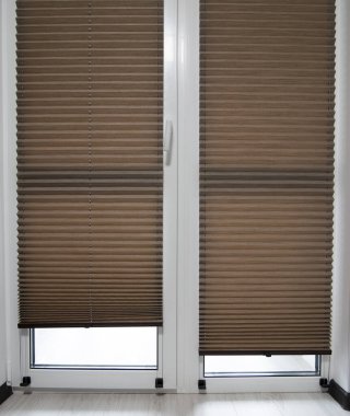 Pleated blinds close up on the window in the interior. Home blinds - cordless pleated modern shades on apartment windows. Brown color fabric.