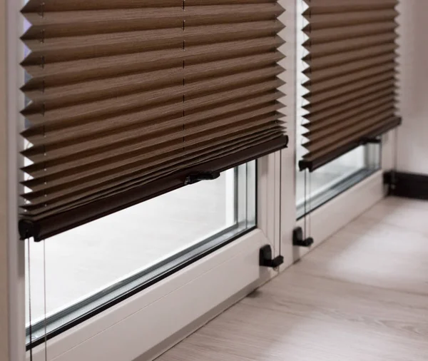 Pleated blinds close up on the window in the interior. Home blinds - cordless pleated modern shades on apartment windows. Brown color fabric.