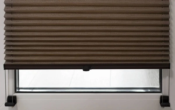 Pleated blinds close up on the window in the interior. Home blinds - cordless pleated modern shades on apartment windows. Brown color fabric.