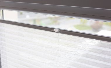 Pleated blinds close up on the window in the interior. Home blinds - cordless pleated modern shades on apartment windows. White color fabric. Bottom up top down pleated curtains.