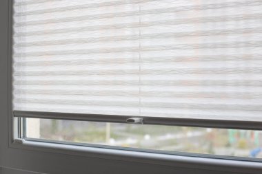 Pleated blinds close up on the window in the interior. Home blinds - cordless pleated modern shades on apartment windows. White color fabric. Bottom up top down pleated curtains.
