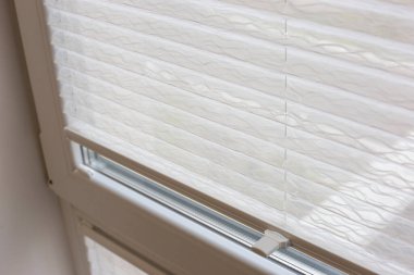 Pleated blinds close up on the window in the interior. Home blinds - cordless pleated modern shades on apartment windows. White color fabric. Bottom up top down pleated curtains.