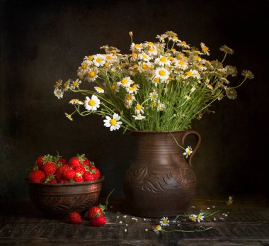 Çilekler ve bir buket papatyayla dolu bir hayat. Kil bir tencerede papatyalar Ahşap bir masa üzerinde Karanlık bir arka plan.