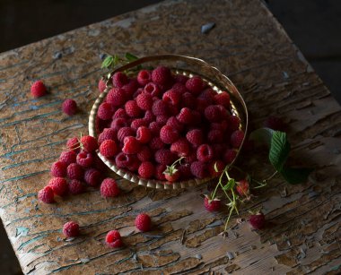 Yapraklı ahududu böğürtlenleri eski ahşap bir masada bakır antika bir tabakta kapanıyor. Üst Manzara. Ahududulu kırsal yaşam. Ağustos hasatı.