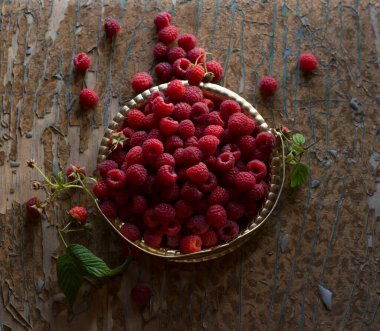 Yapraklı ahududu böğürtlenleri eski ahşap bir masada bakır antika bir tabakta kapanıyor. Üst Manzara. Ahududulu kırsal yaşam. Ağustos hasatı.