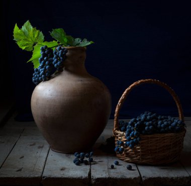 Koca bir sürahi ve yabani üzümle dolu bir hayat. Parlak yeşil yapraklı bir demet mavi üzüm bir sürahide yatıyor. Bir sürü üzüm hasır sepetin içinde, tahta bir masada bir sürahinin yanında yatıyor. Ülke biçimi.