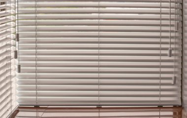 Alüminyum panjurlar. Metalden yapılmış. Venedik perdeleri pencereyi kapatıyor. Gümüş rengi. Güneşli bir günde kapalı yatay panjurlar.