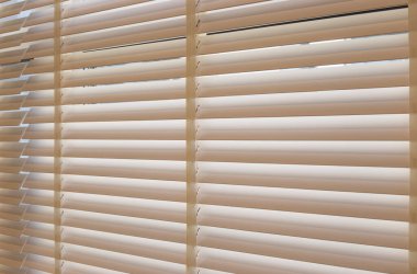 Wood blinds closeup in the interior. Automatic venetian blinds beige color on large windows. Wooden slats 50mm wide. Wood floor, beige walls.