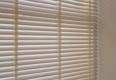 Wood blinds closeup in the interior. Automatic venetian blinds beige color on large windows. Wooden slats 50mm wide. Wood floor, beige walls.