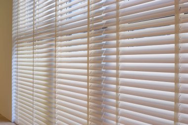 Wood blinds closeup in the interior. Automatic venetian blinds beige color on large windows. Wooden slats 50mm wide. Wood floor, beige walls.