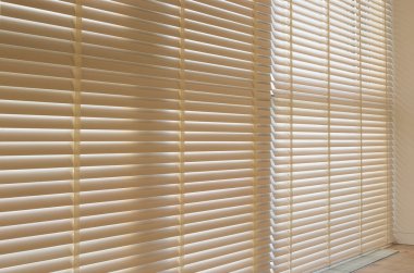 Motorized wood blinds in the interior. Automatic venetian blinds beige color on large windows. Wooden slats 50mm wide. Wood floor, beige walls.