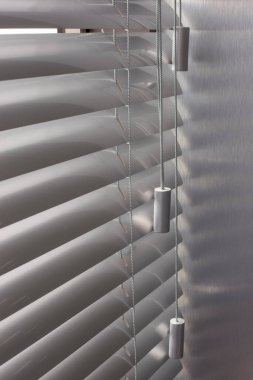 Ofis pencerelerinde alüminyum panjurlar var. Metalden yapılmış. Venedik perdeleri pencereyi kapatıyor. Gümüş rengi. Güneşli bir günde yatay jaluziler kapalı. Modern güneş koruması ve pencere dekorasyonu. Seçici odak.