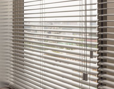 Ofis pencerelerinde alüminyum panjurlar var. Metalden yapılmış. Venedik perdeleri pencereyi kapatıyor. Gümüş rengi. Arka planda şehir manzarası var. Modern güneş koruması ve pencere dekorasyonu. Seçici odak.