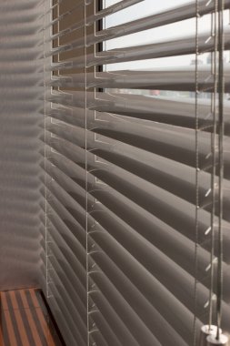 Ofis pencerelerinde alüminyum panjurlar var. Metalden yapılmış. Venedik perdeleri pencereyi kapatıyor. Gümüş rengi. Güneşli bir günde yatay jaluziler kapalı. Modern güneş koruması ve pencere dekorasyonu.