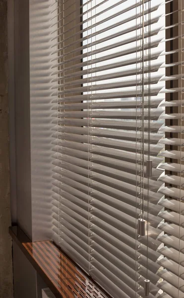 Aluminum blinds on the office windows. Made from metal. Venetian blinds closeup on the window. Silver color. City landscape is in the background. Modern sun protection and window decoration. Selective focus.