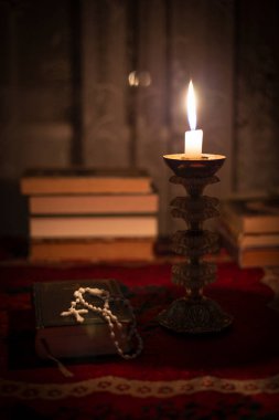 Dua kitabında tespih, eski bir şamdanda mum ve pencerenin yanında kitaplarla dolu bir hayat. Masanın üzerinde eski bir masa örtüsü var. Hıristiyanlık kavramı. Namaz vakti..