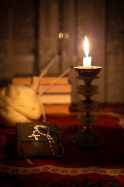 Dua kitabında tespih, eski bir şamdanda mum ve pencerenin yanında kitaplarla dolu bir hayat. Masanın üzerinde eski bir masa örtüsü var. Hıristiyanlık kavramı. Namaz vakti..