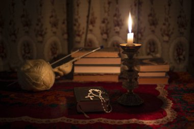 Dua kitabında tespih, eski bir şamdanda mum ve pencerenin yanında kitaplarla dolu bir hayat. Masanın üzerinde eski bir masa örtüsü var. Hıristiyanlık kavramı. Namaz vakti..