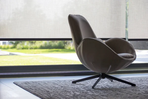 İç taraftaki pencerenin perdeleri büyük boyutlarda. Otomatik güneş gözlüğü, keten desenli kumaş. Büyük bir pencerenin önünde halının üzerinde bir sandalye var. Dışarısı bahçe manzaralı..