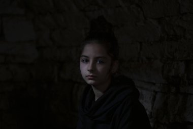 War in Ukraine. A child in a basement, looking at the camera. A beam of light falls on her face. Portrait of the little girl in the dungeon with dark background. Pray for Ukraine.