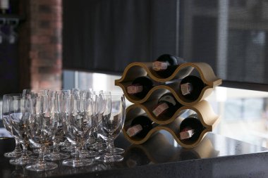Roller blinds on the window in the restaurant interior. Motorized solar shades, black screen fabric. A control panel for blinds is on the bar counter of the restaurant, glasses and bottles of wine. 