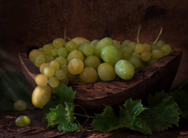 Ahşap arka planda, tahta bir kasede taze üzümlerle dolu bir hayat. Masanın üzerinde yeşil üzüm yaprakları var. Hollandalı tarzı böğürtlenli hayat. 