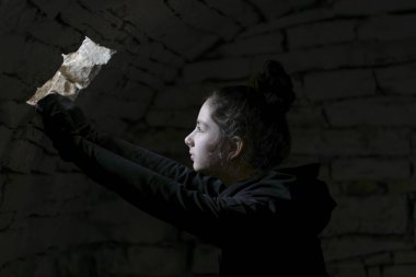 Bodrumda küçük bir pencereden bakan bir çocuk. Yüzüne bir ışık hüzmesi düştü. Zindandaki karanlık geçmişli küçük kızın portresi..