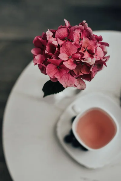 a hydrangea flower in a vase and a cup of tea on the table