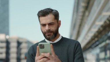İş adamı sokakta yürürken cep telefonuna bakıyor
