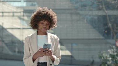 Sokakta akıllı telefon kullanan Afrikalı Amerikalı bir iş kadını.