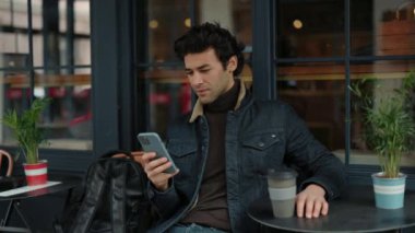 Kafe terasında otururken akıllı telefon kullanan genç hippi.