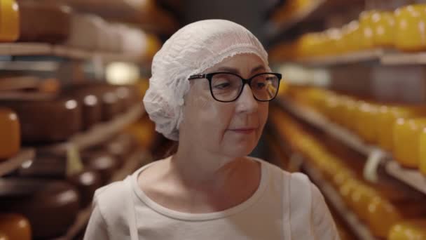 Idősebb nő áll a raktárban polcokkal sajt — Stock videók