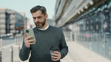 Orta yaşlı işadamı yürürken akıllı telefon kullanıyor.