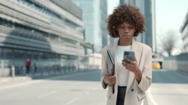 Belgeleri taşıyan ve açık havada cep telefonu kullanan kendinden emin Afro-Amerikan kadın.